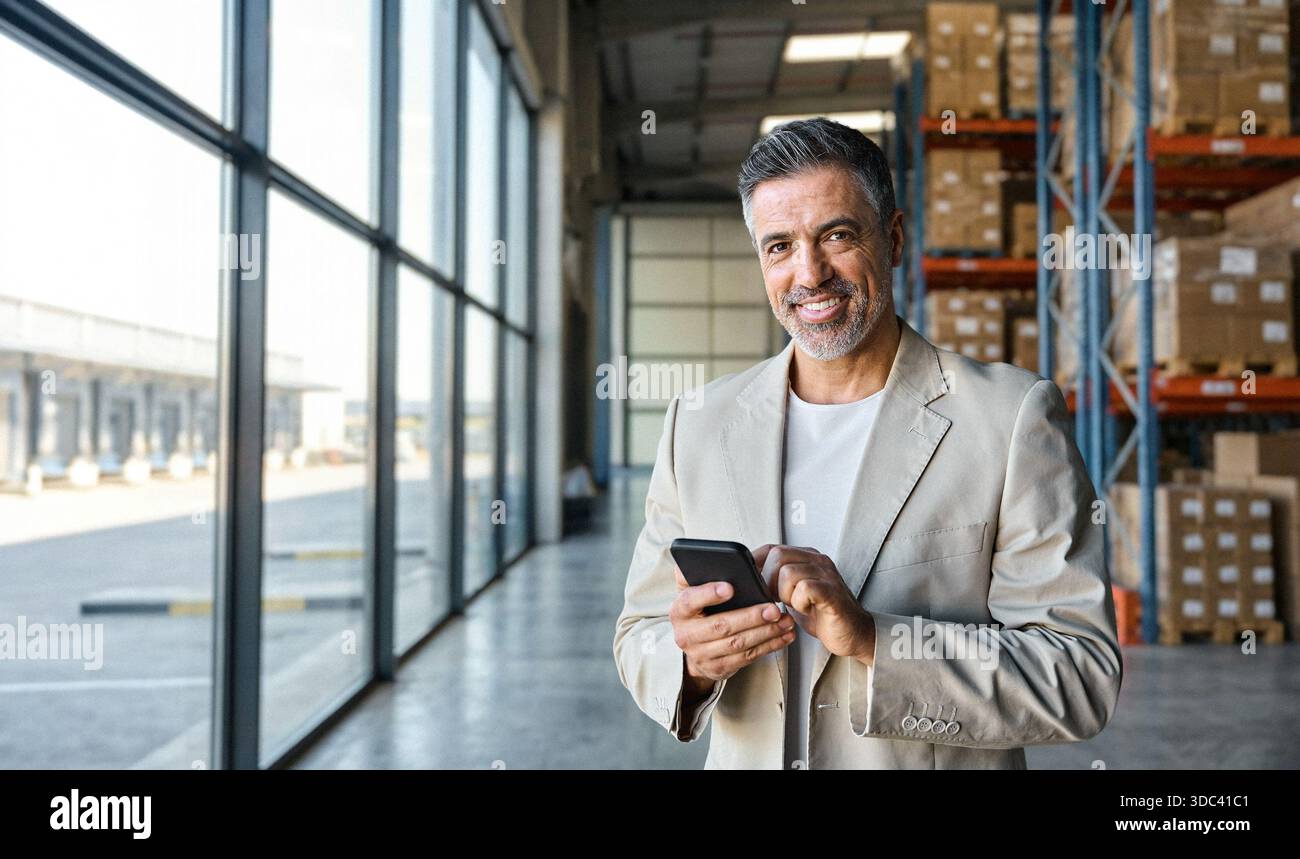 Warehouse manager standing near cardboard boxes using smartphone. Stock Photo