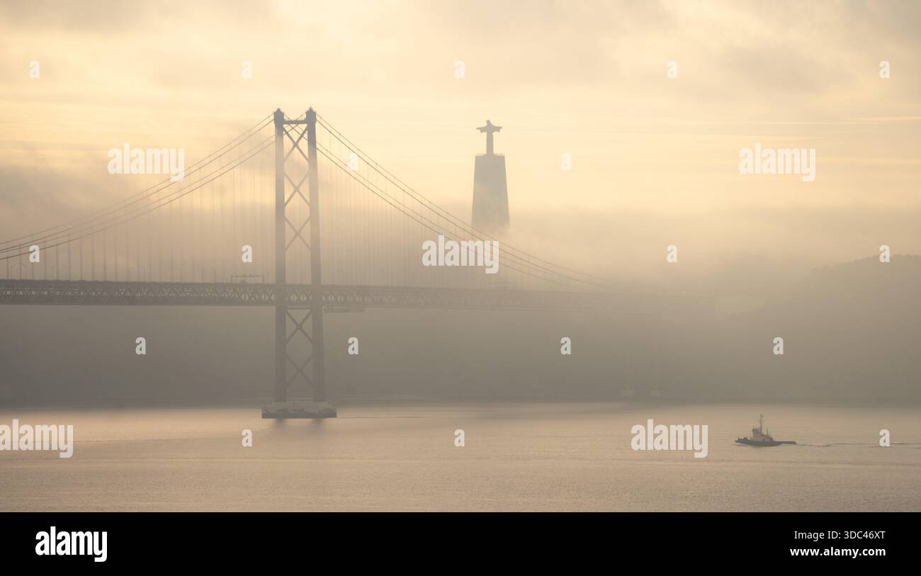 Lissabon, Portugal – Ponte 25 de Abril und Cristo Rei im Morgennebel über dem Tejo. ein Schlepper kehrt zum Hafen zurück. Stock Photo