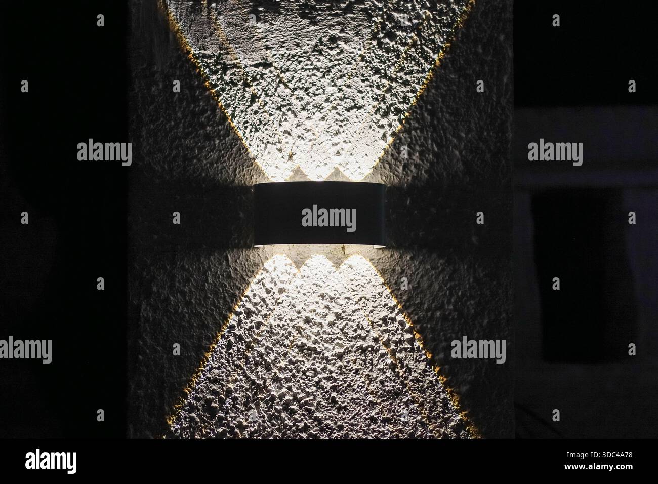 Sleek wall lamp emitting dual directional light on textured plaster in nighttime setting Stock Photo