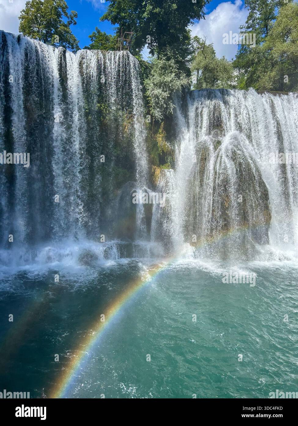 Scenic waterfall landscape in Jajce featuring cascading water, emerald river, and a soft rainbow in the spray, symbolizing natural beauty, travel, and - Smartphone Captured Stock Image