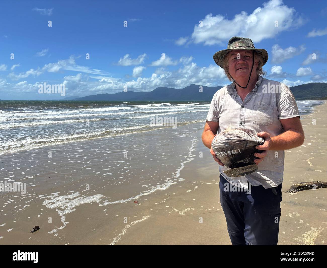 Inventor of the coconut drifter Dennis Stanley after retrieving one that washed ashore on Wungu Beach, Yarrabah Aboriginal Shire, on the shores of the - Smartphone Captured Stock Image