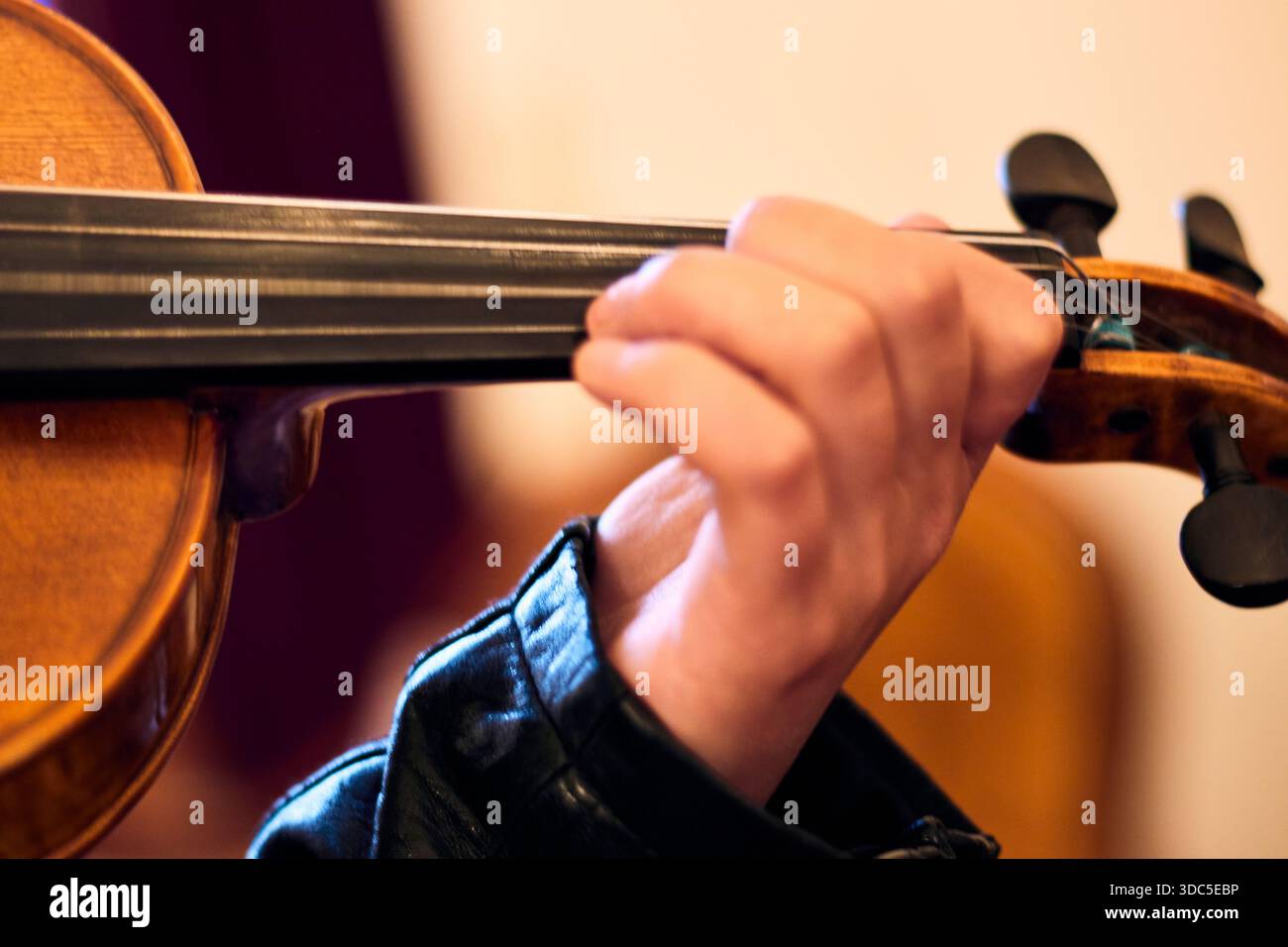 View of a young white woman's hands playing a violin in a classical hall, moving and adjusting her fingers on the violin strings, playing musical note Stock Photo
