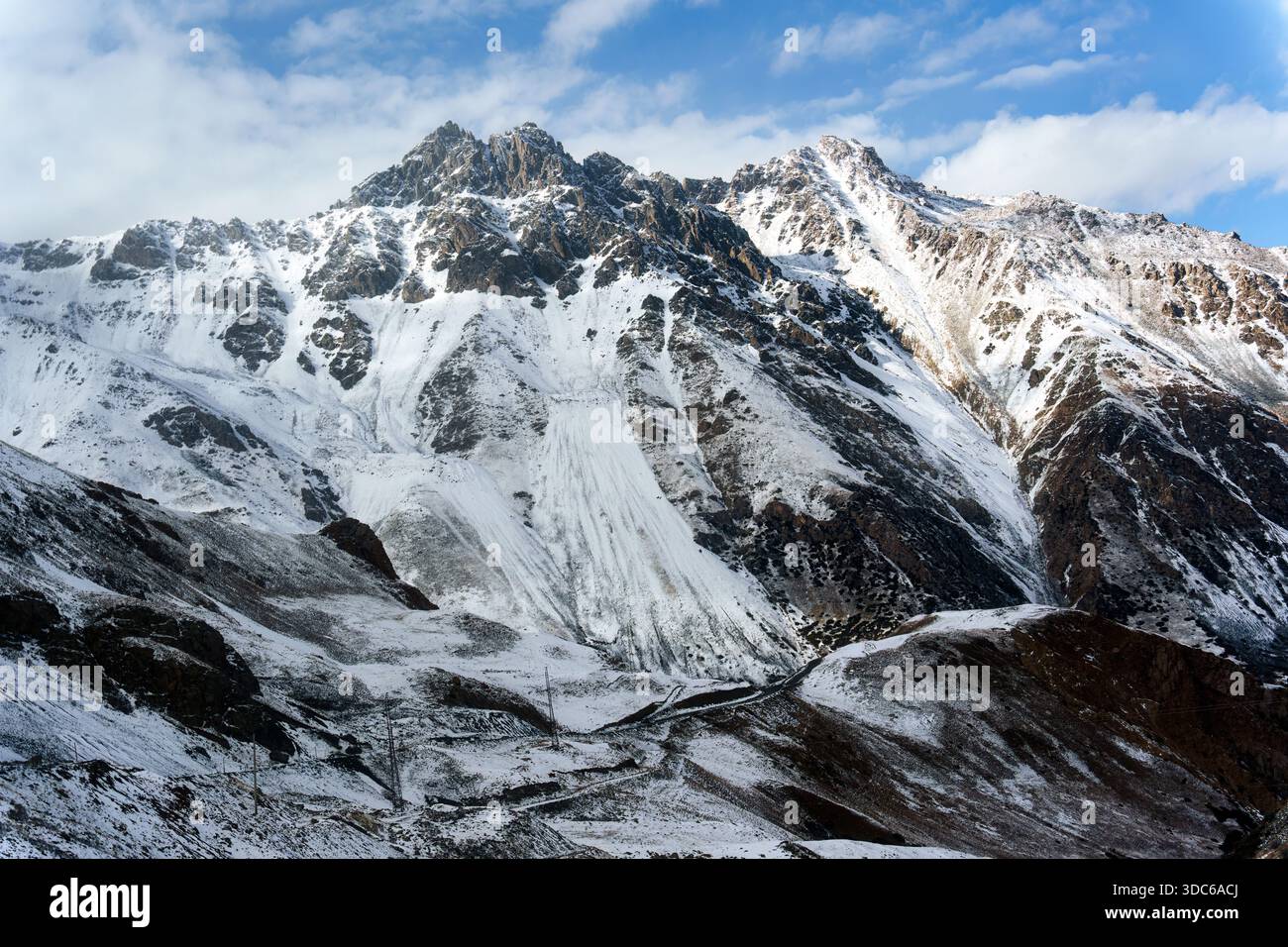 Scenic rugged snowy steep mountain with mountain pass and dirt road in remote valley at Kyrgyzstan Stock Photo