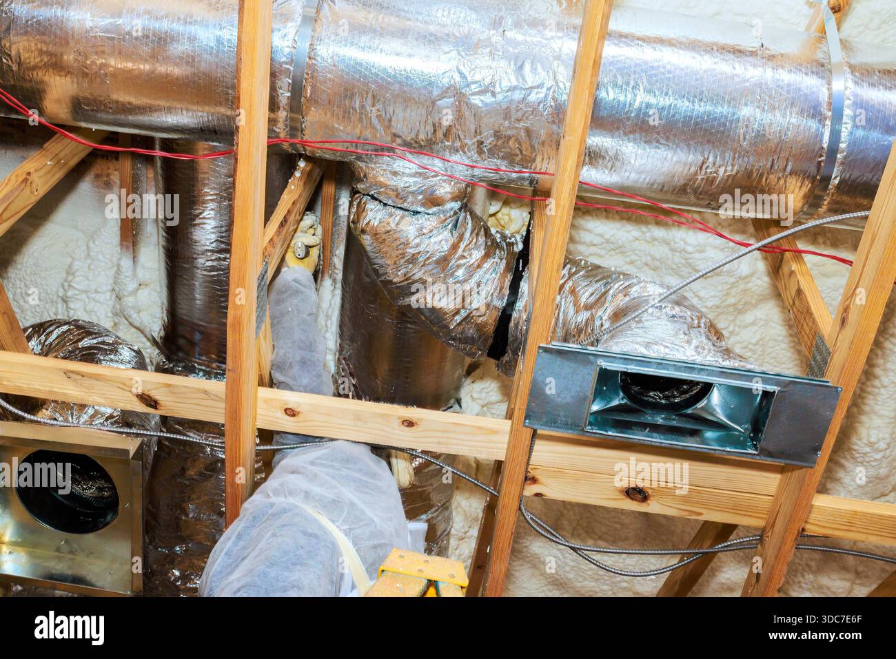 Workers are installing metal ducts in an attic, ensuring proper ventilation for new home. Stock Photo