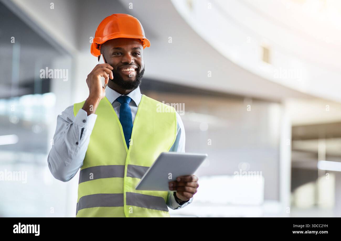 Construction Worker Talking on Phone While Using Tablet in Office Setting Stock Photo