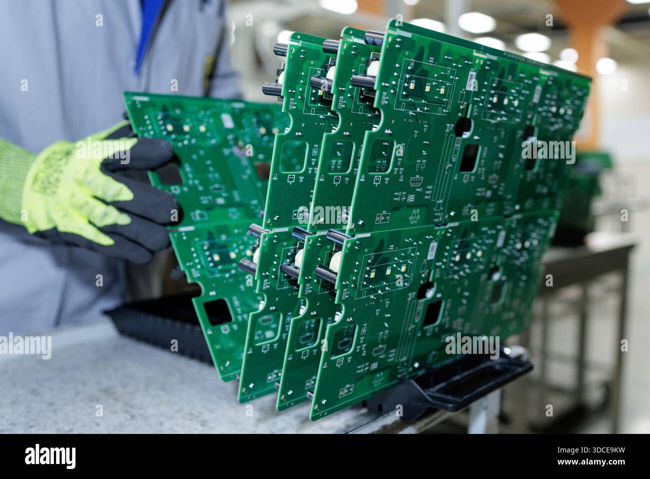 Factory worker in protective gloves handling large green printed circuit board panels during electronics assembly process Stock Photo