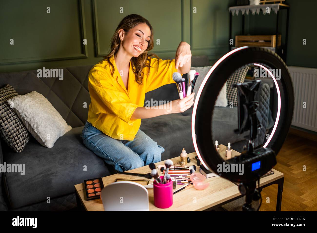 Influencer recording a beauty routine at home. She is using ring light and smartphone. Stock Photo