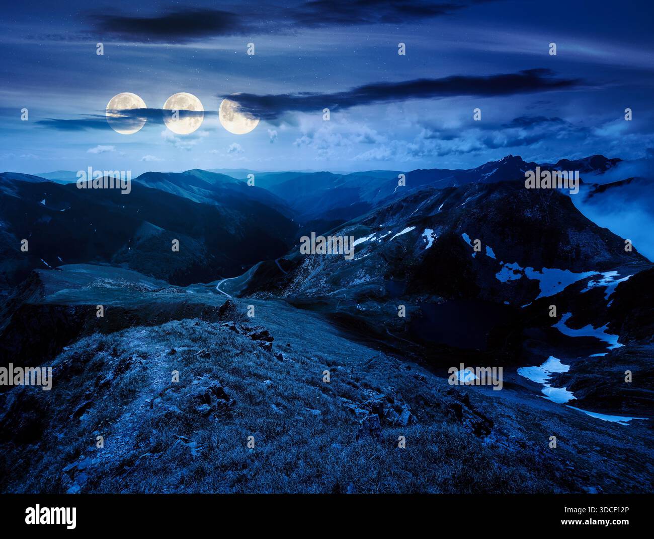 beautiful landscape of mountains at night. lovely summer scenery with cloudy sky in full moon light. Lake down the hill. grass and snow on alpine slop Stock Photo