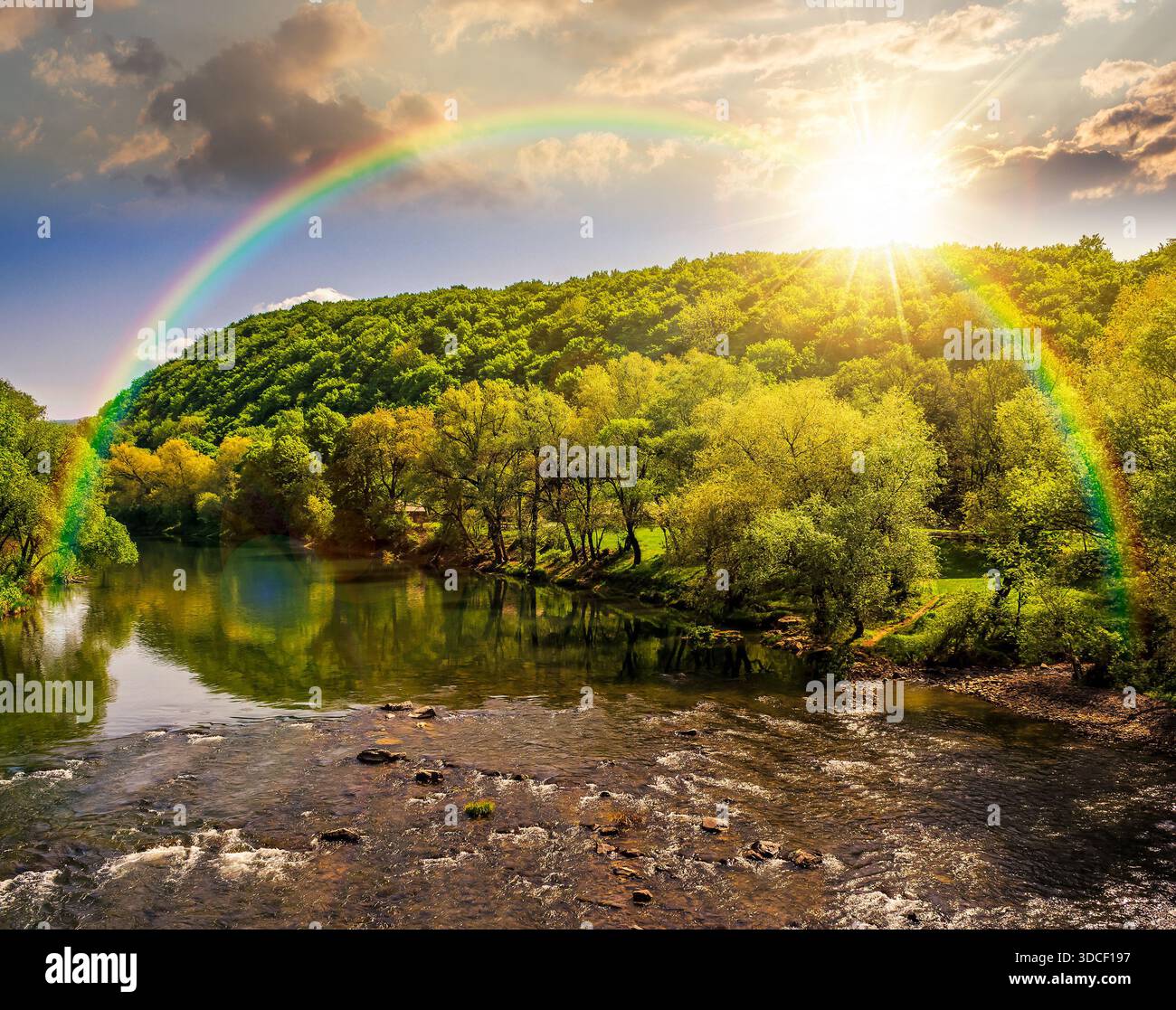 River flows among green forest near mountain at sunset. picturesque nature of a serene spring landscape in evening light. deciduous trees reflection. Stock Photo