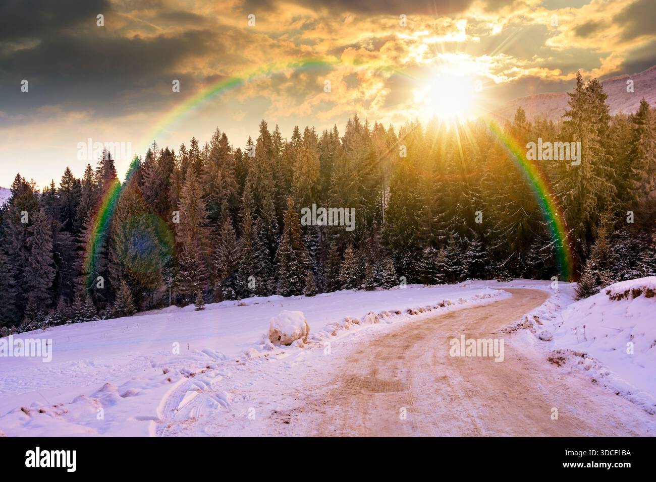 winter landscape with snow covered country road winding through fir forest in mountains at sunset. alpine countryside of in evening light. timeless no Stock Photo