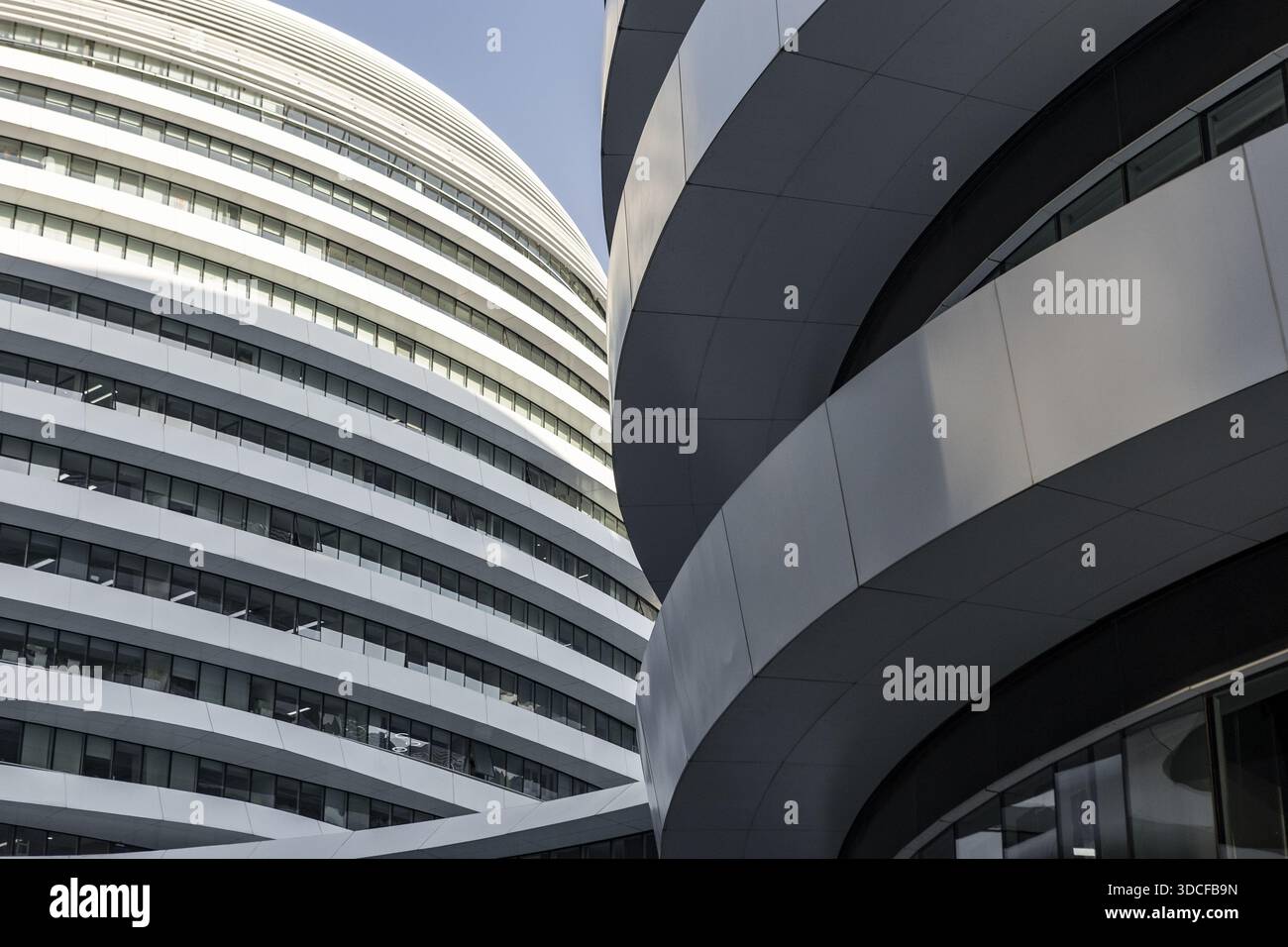 View of striking modern architecture with curved white panels against a bright blue sky, creating a dynamic contrast in Beijing, China Stock Photo