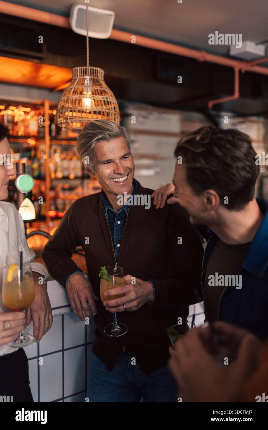 Happy friends laughing while enjoying near bar counter at restaurant ...