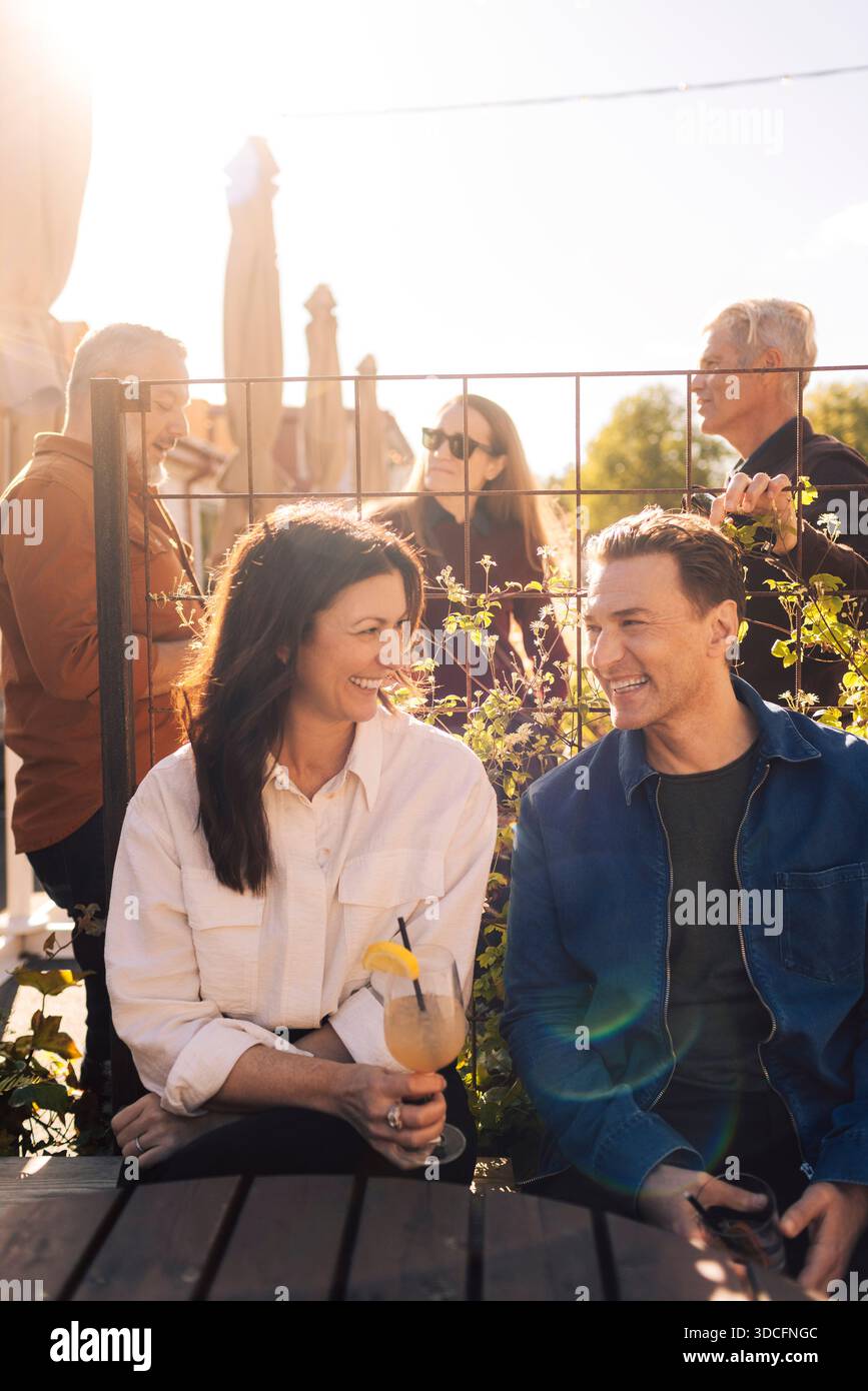 Happy mature friends talking with each other while sitting outdoors in cocktail party Stock Photo