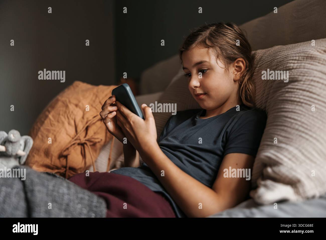 Girl using smart phone while lying on bed in home Stock Photo