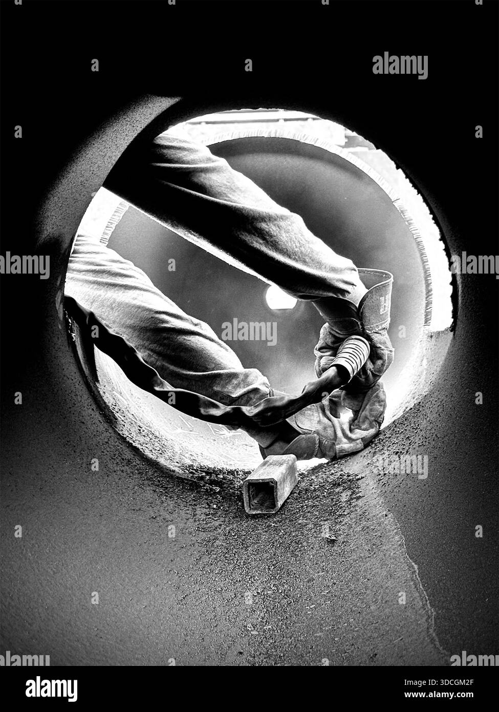 Black and white photograph showing a worker’s gloved hands operating a tool inside a large metal pipe. The image is taken from within the pipe - Smartphone Captured Stock Image