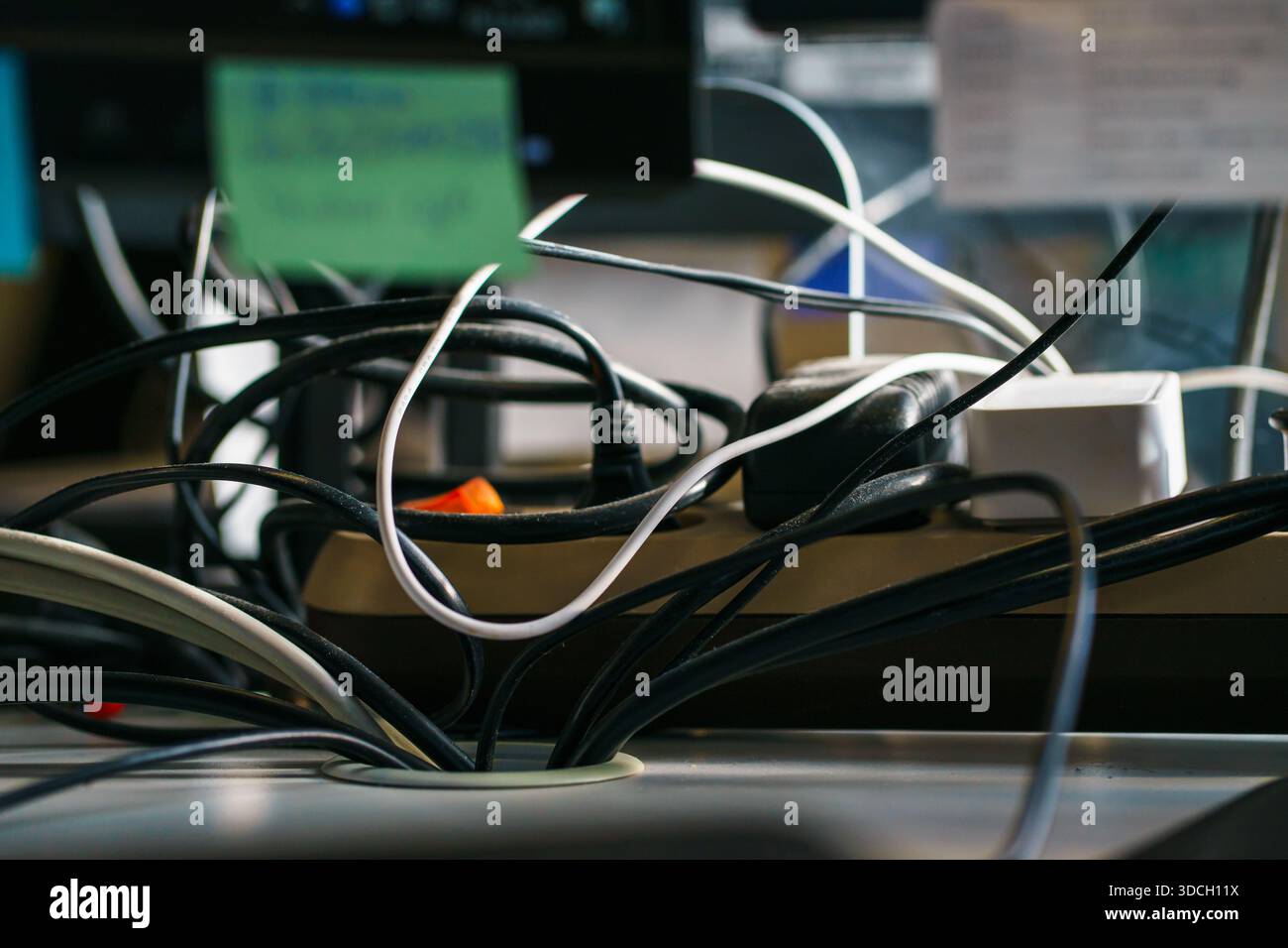 Tangled power cords, adapters, and chargers on desk symbolize cable clutter, technology overload, home office chaos, and workplace organization issues Stock Photo