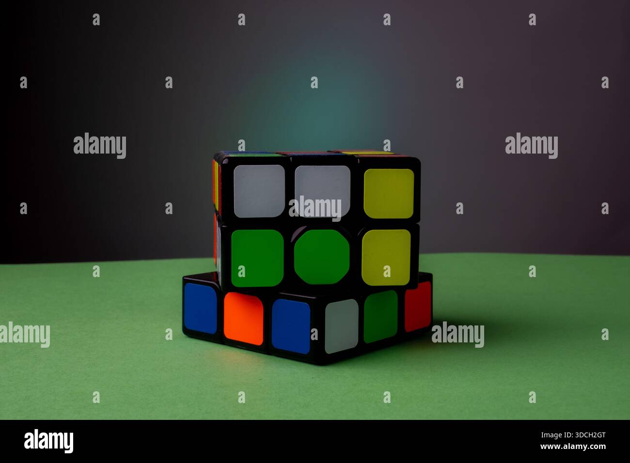 Partially solved Rubik's Cube on a green surface with a dark background. Stock Photo