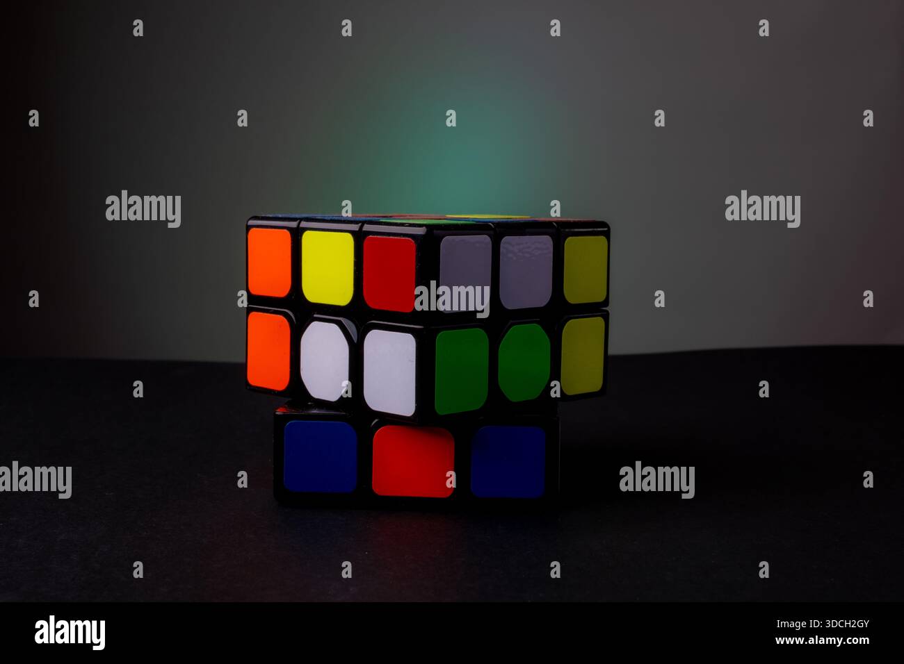 A partially solved Rubik's Cube on a dark surface with a gradient background. Stock Photo