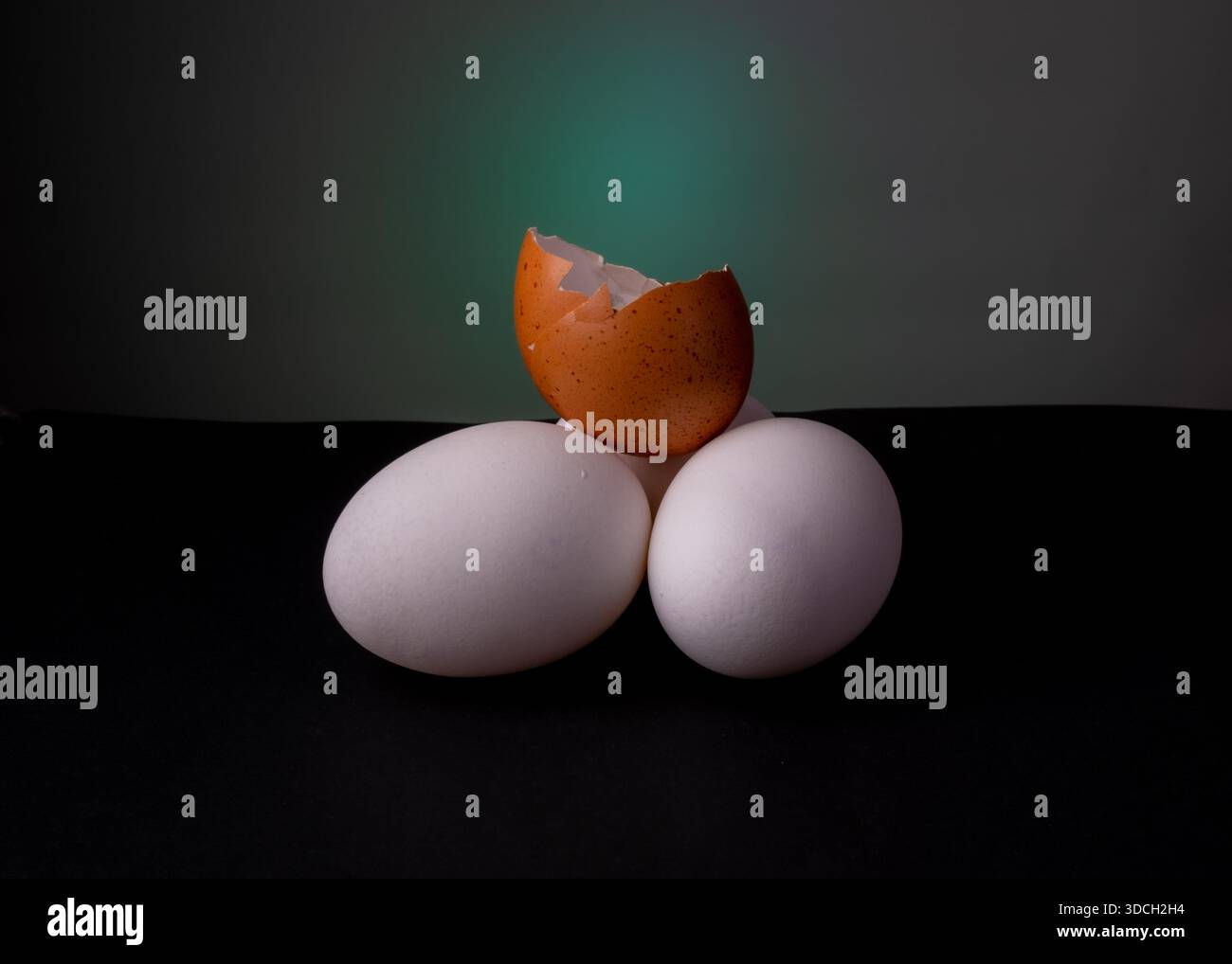 Three eggs arranged with a broken brown eggshell on top, set against a dark background. Stock Photo