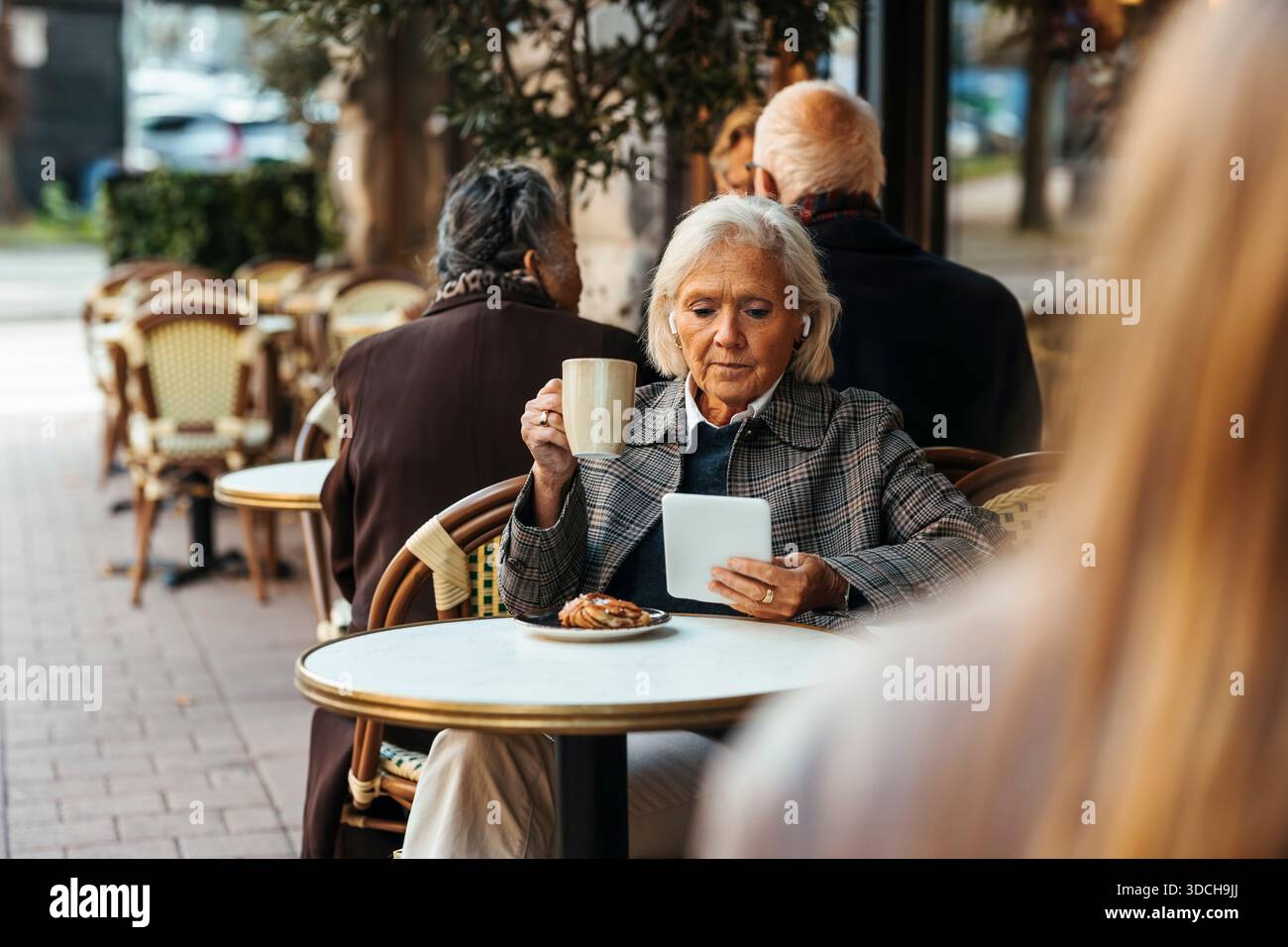 Senior woman having coffee while using tablet PC at sidewalk cafe Stock Photo