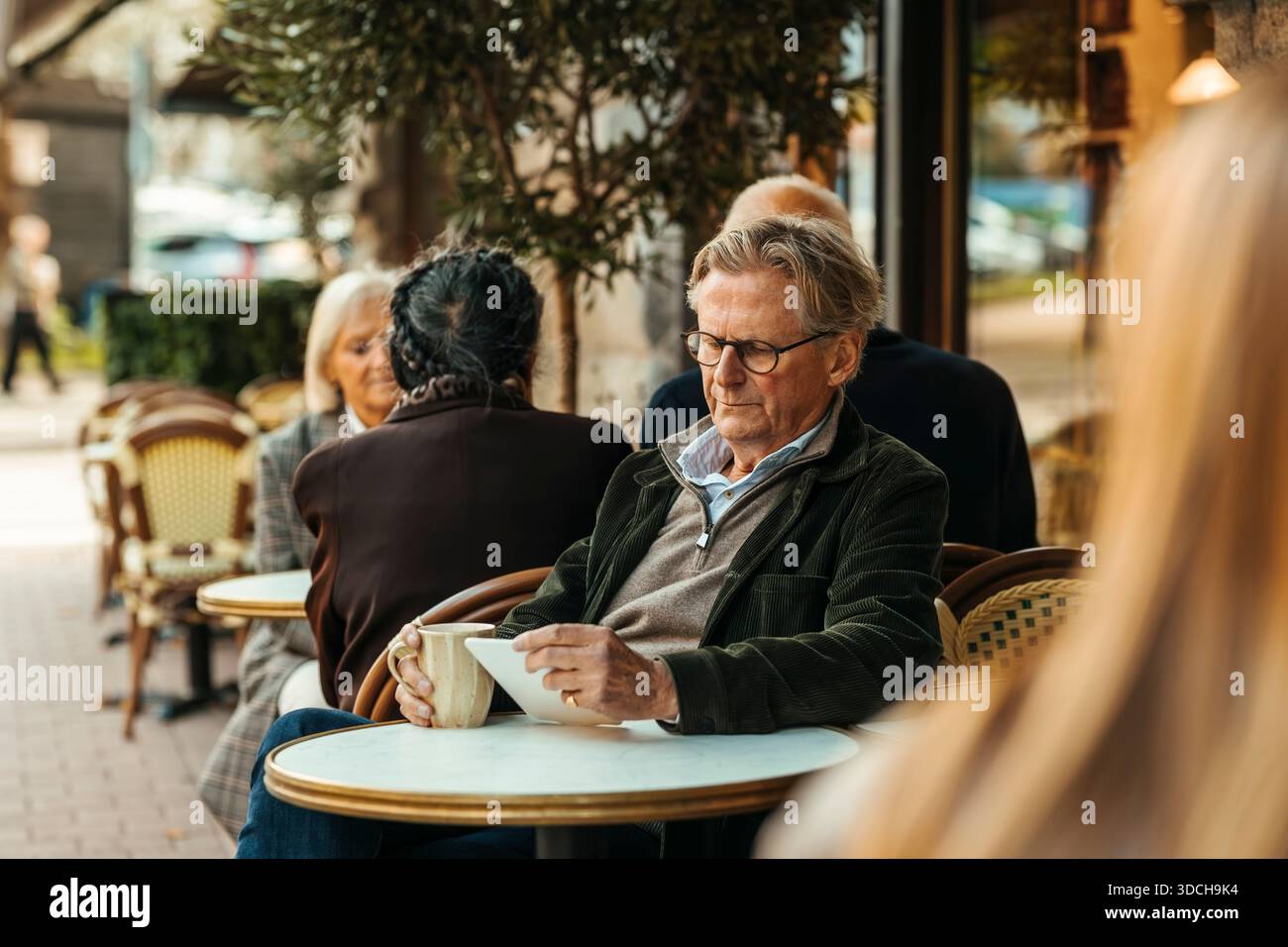 Senior man using digital tablet while sitting at sidewalk cafe Stock Photo