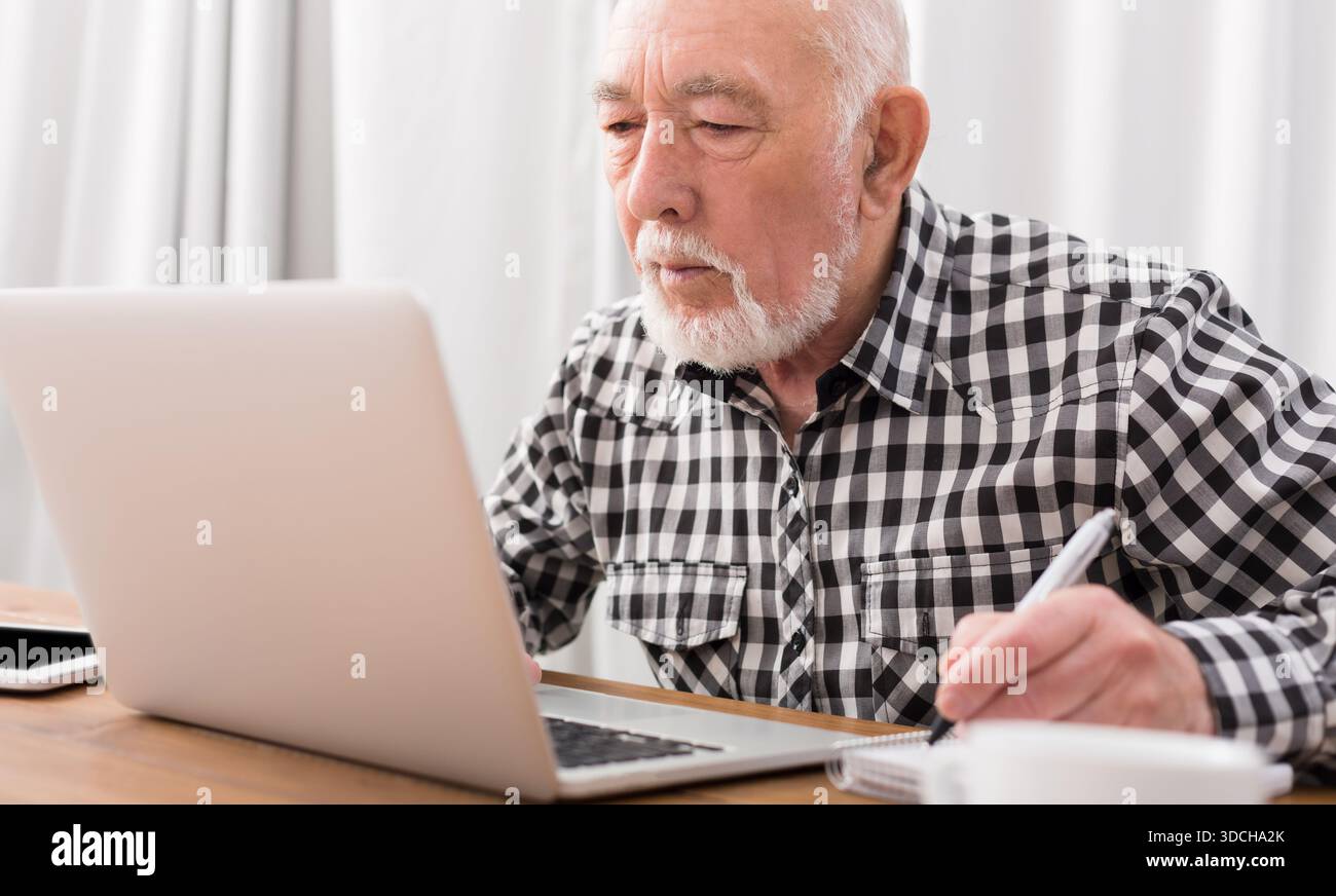 Mature man using laptop and writing in notepad Stock Photo