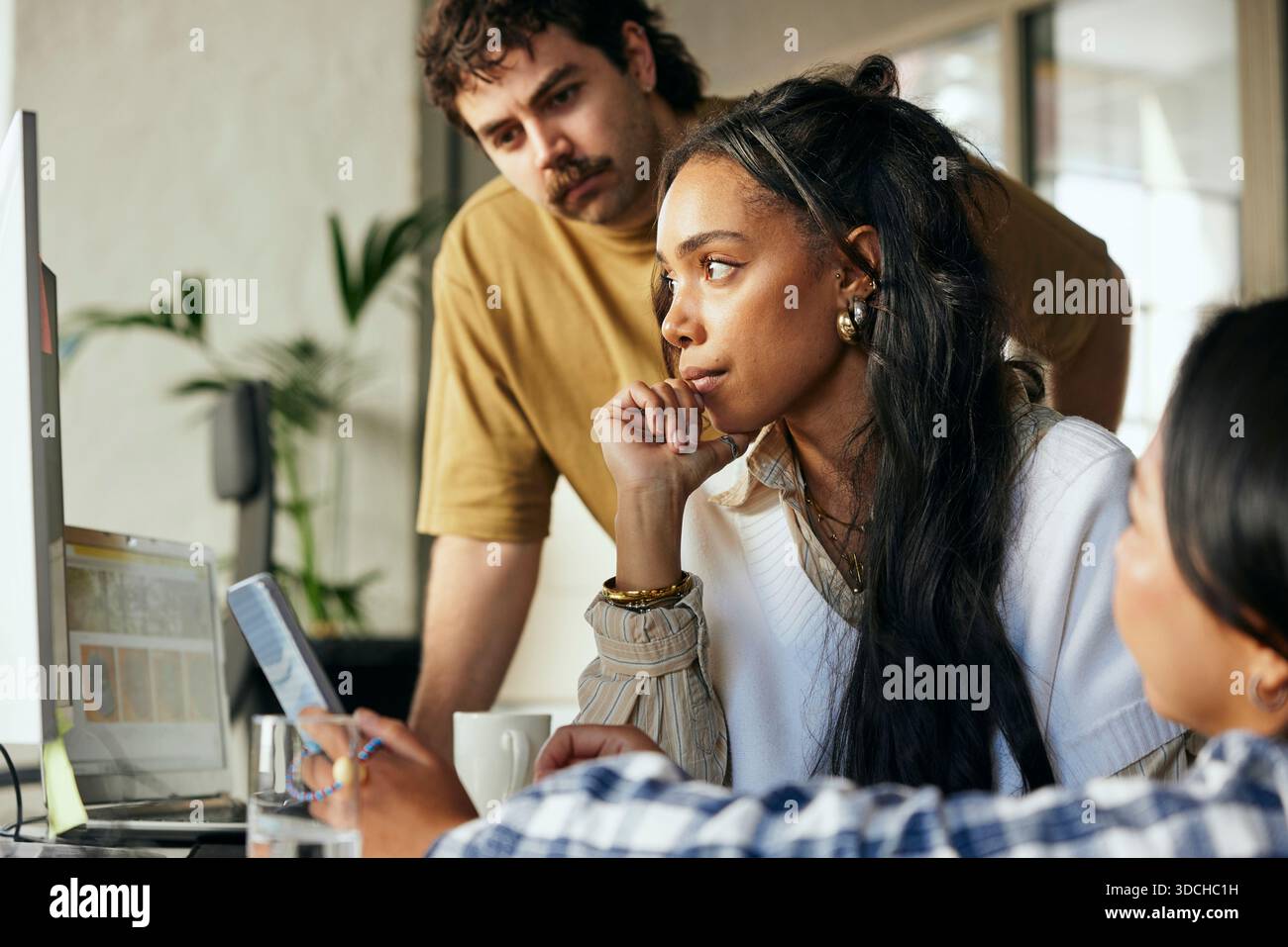 Concentrated female programmer working with colleagues on desktop PC in startup office Stock Photo