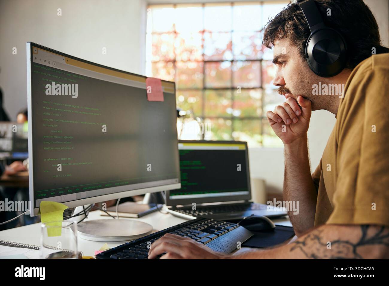 Focused male programmer wearing wireless headphones coding on computer in startup office Stock Photo