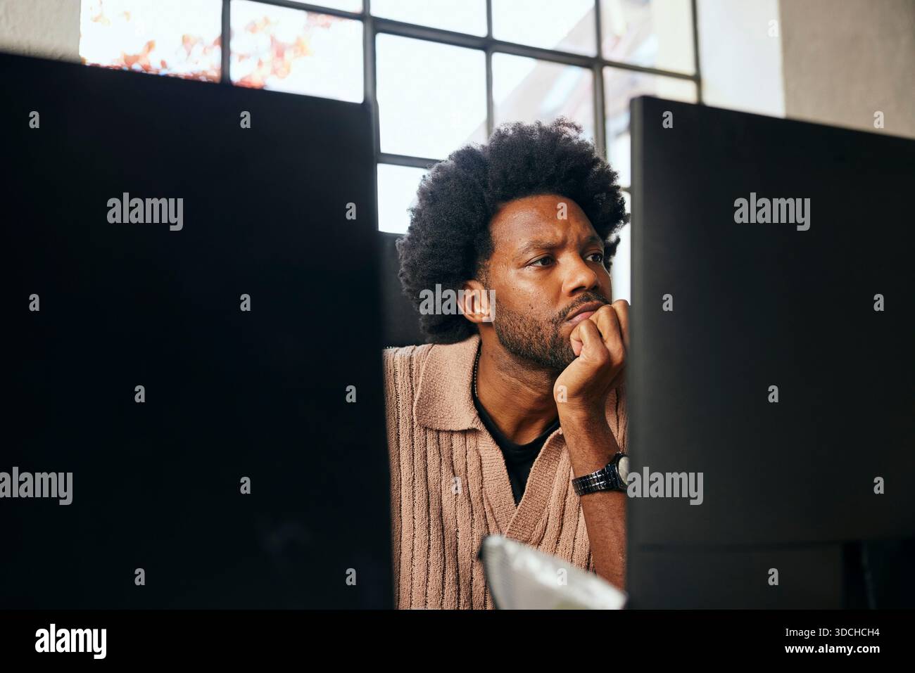 Curly haired male tech professional leaning on elbow while working in startup office Stock Photo