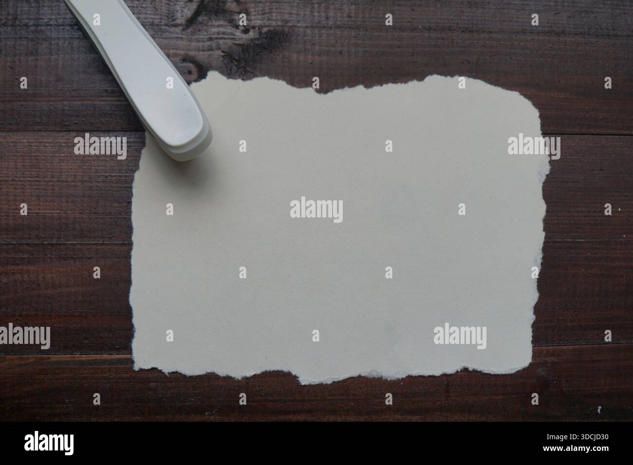 A white stapler placed on torn white paper atop a dark wooden surface. Stock Photo