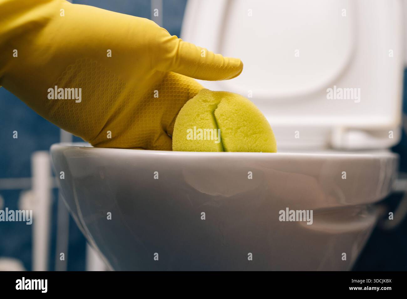 Hand in yellow rubber glove cleaning toilet bowl with green sponge ...
