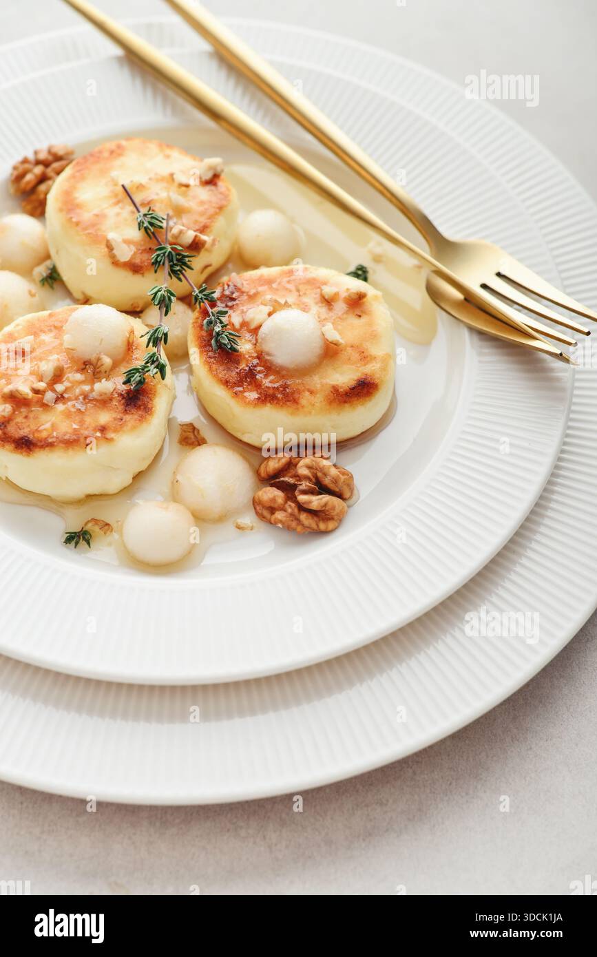 White plate with cottage cheese pancakes, syrniki, curd fritters served with pear balls, walnut and honey on light background, top view Stock Photo