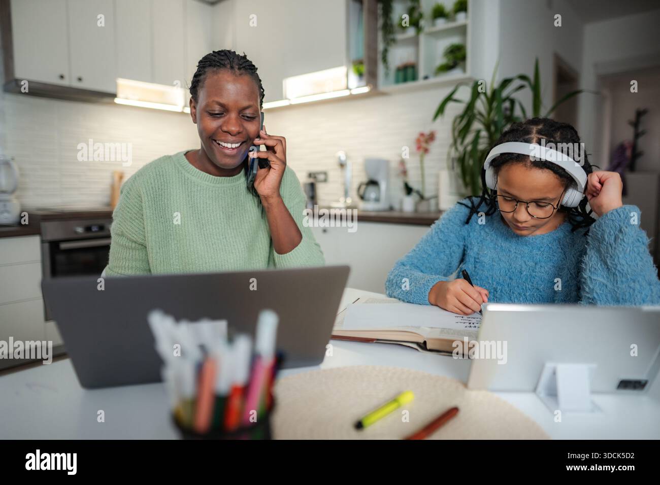 Mother multitasking working from home while daughter remote learning Stock Photo