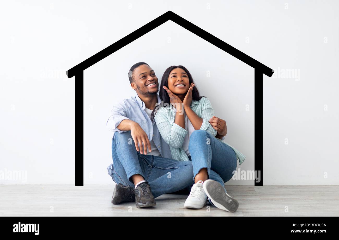 Excited african american spouses sitting near white wall with drawn house Stock Photo