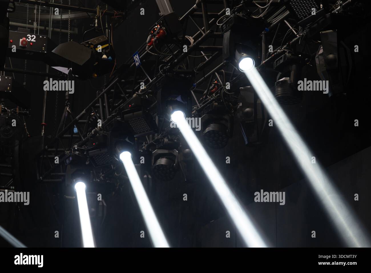 Stage lighting equipment illuminates a dark venue, with multiple moving head lights emitting strong white beams, all mounted on a robust metal truss Stock Photo