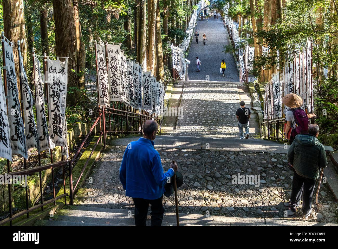 Visitors walk along the flag-lined rocky path of the Oyunohara Approach to Kumano Hongū Taisha, Tanabe, Wakayama Prefecture, Japan. The path leads up from the old riverbed to the shrine. Stock Photo