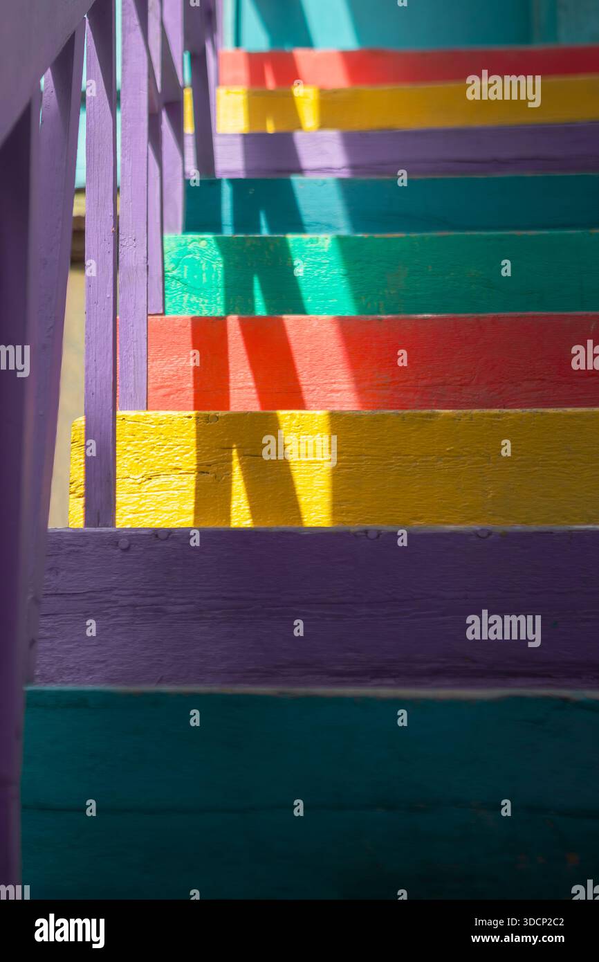 Rainbow wooden stairs with purple railing cast sharp diagonal shadows ...