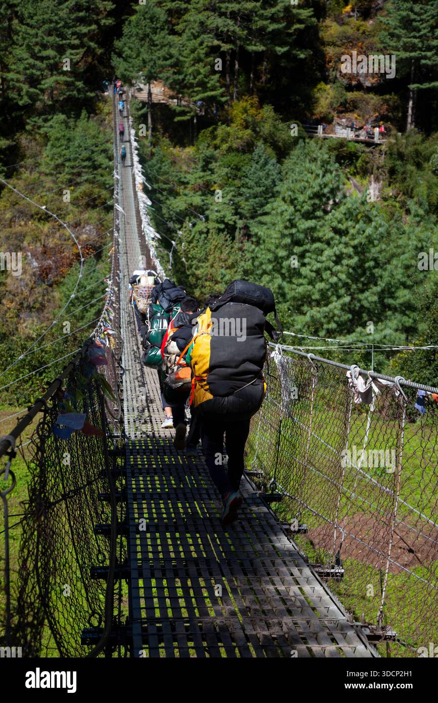 Nepalian Porter carrying heavy load on his back going along the bridge ...