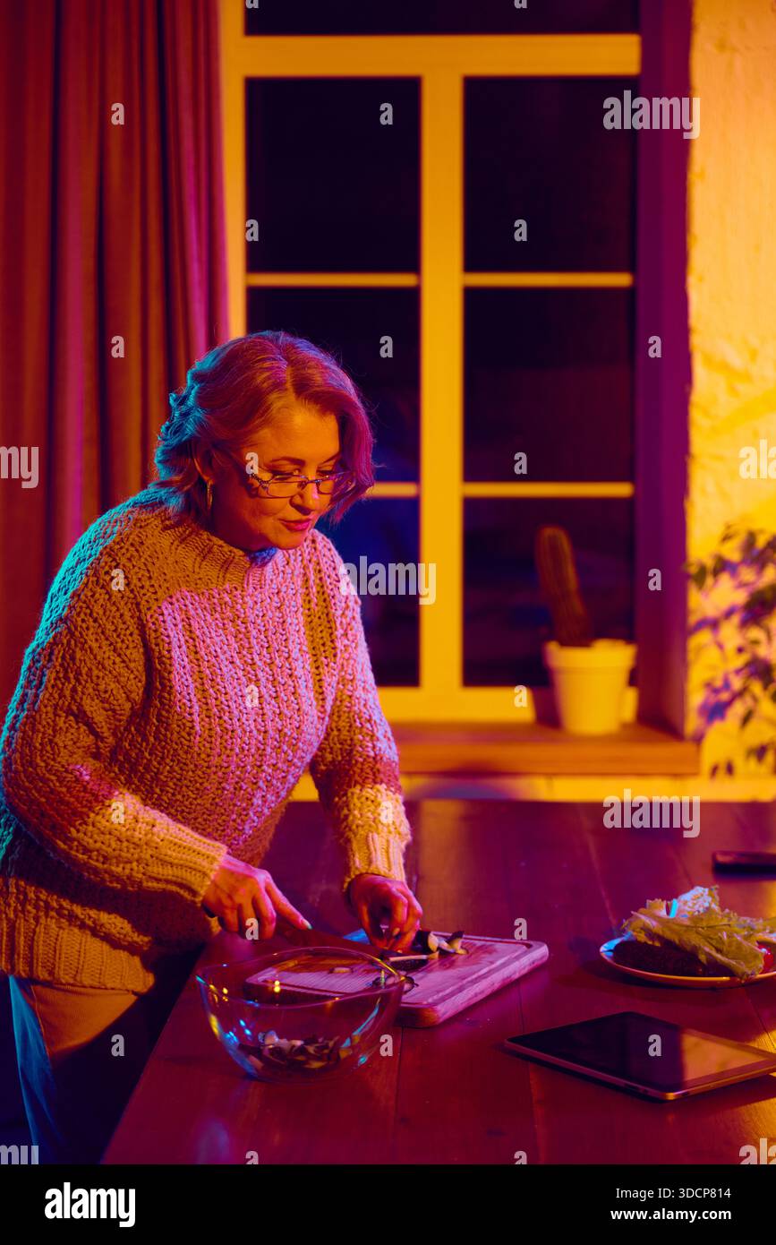 Senior woman cooking while interacting with virtual assistant interface Stock Photo
