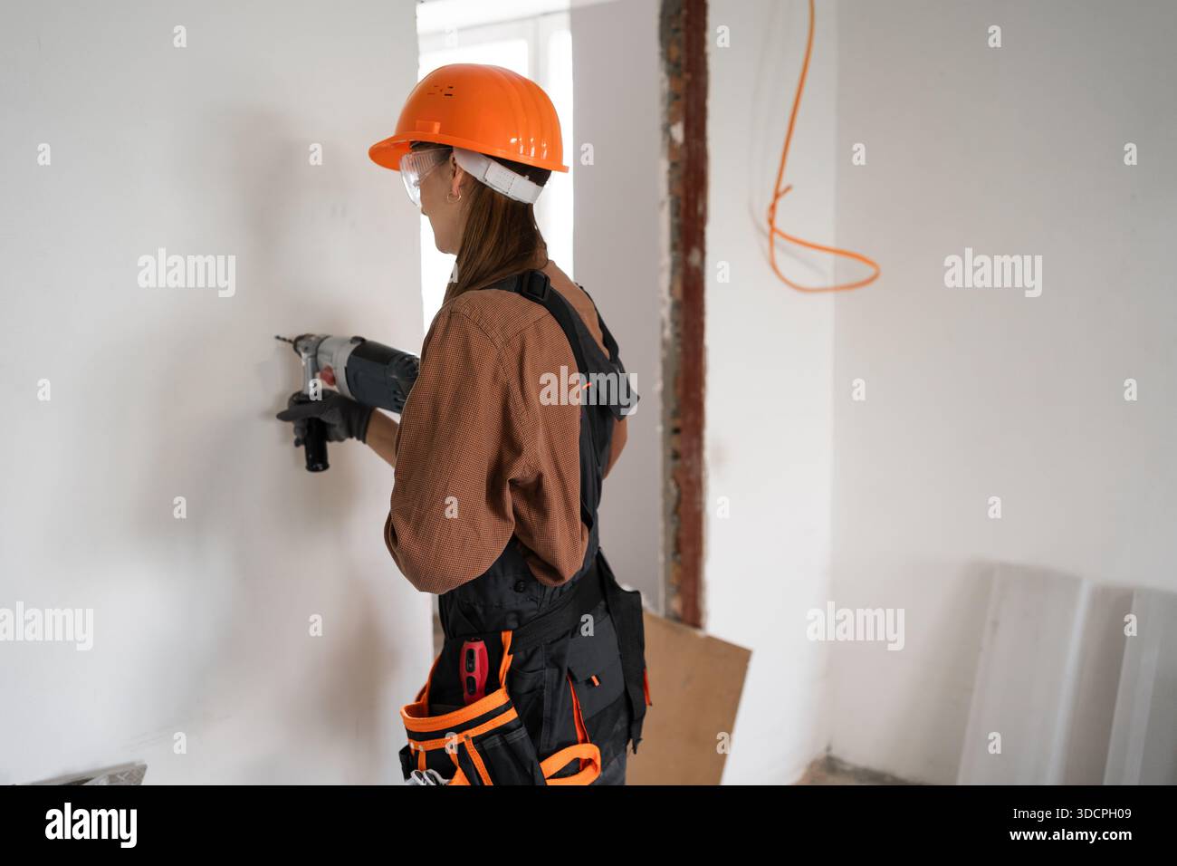 Female construction worker using hammer drill. Builder woman with pneumatic hammer drill perforator making hole in wall. copy space Stock Photo