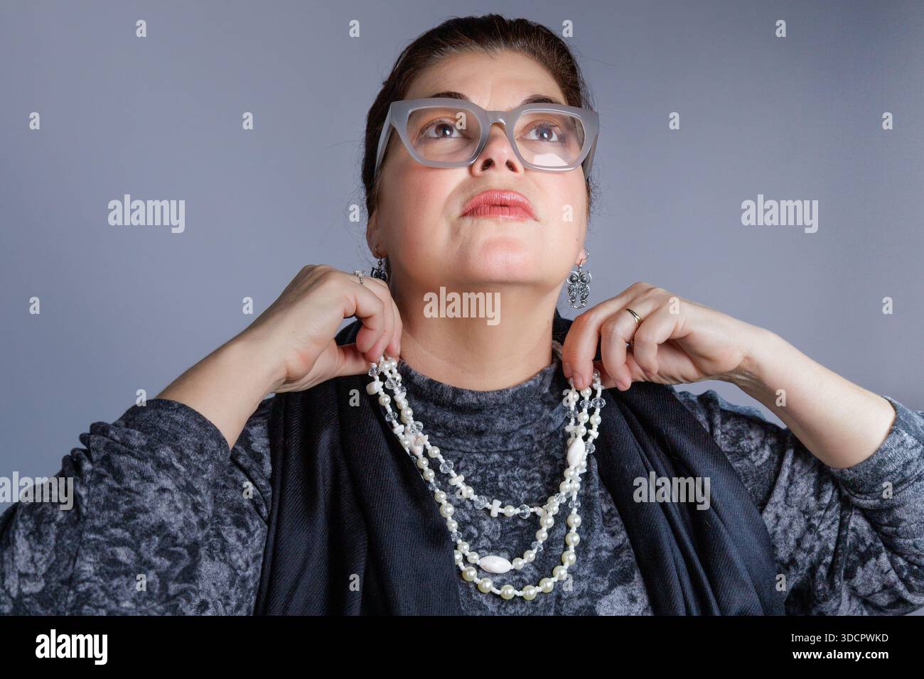 Woman wearing glasses adjusting a layered pearl necklace while looking upward. Stock Photo