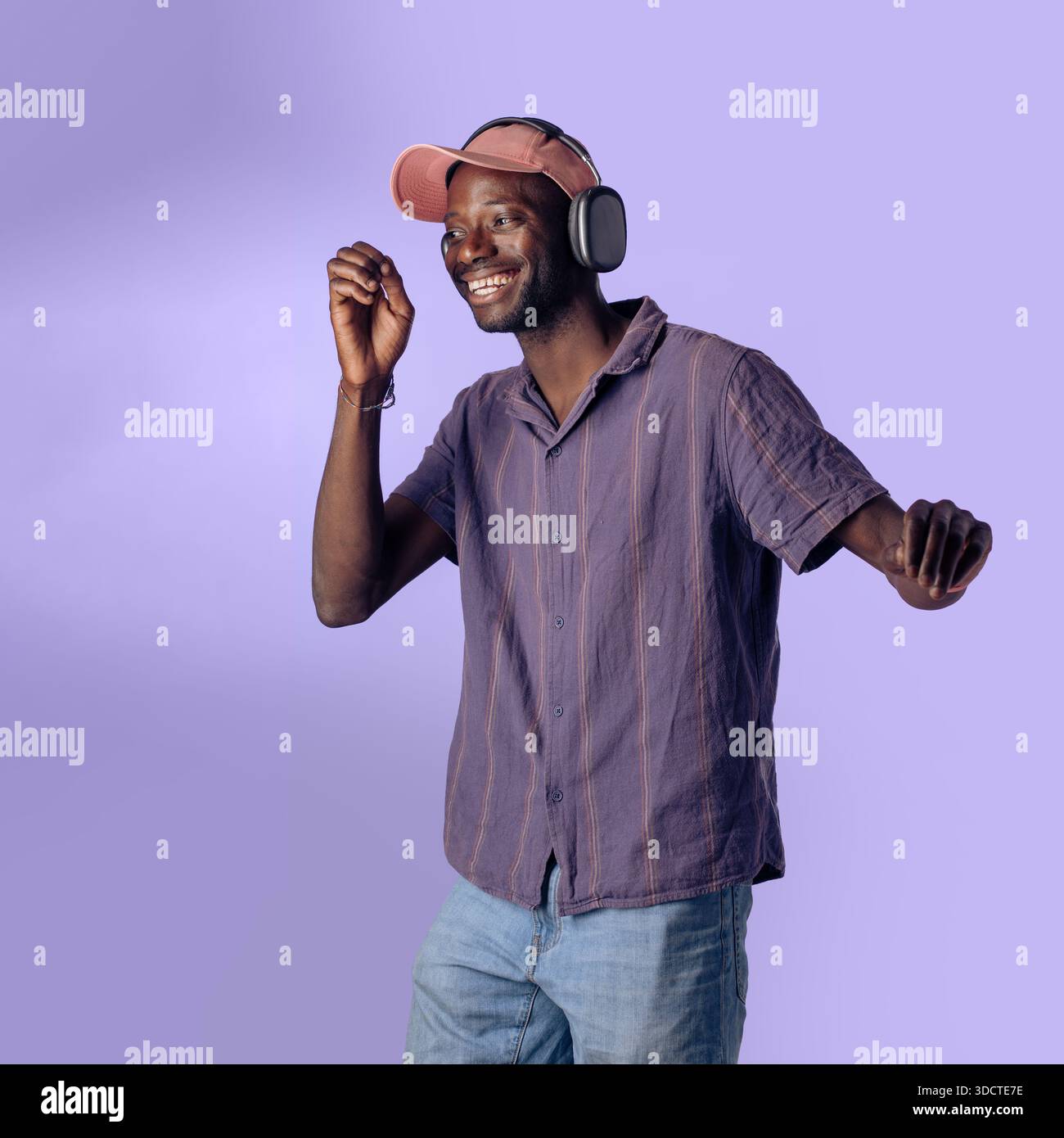 Happy young Black man dancing while listening to music with wireless headphones in a studio setting. Relaxed lifestyle, joy, freedom and modern music Stock Photo