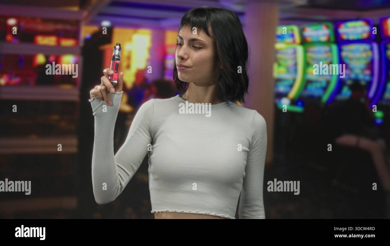 vape ranking 2025 Smiling young woman holding vape with freckled face in colorful slot  machine area of casino building; confidence Stock Photo