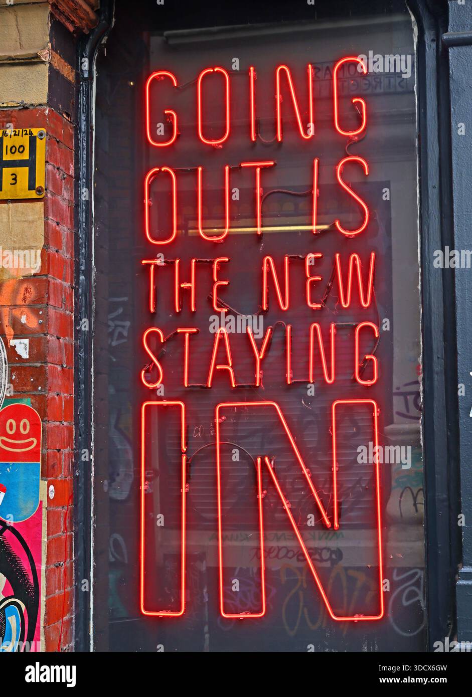 Red neon sign reading “Going Out Is The New Staying In” displayed in a window on Thomas Street in Manchester’s Northern Quarter, at 30–32 Thomas St Stock Photo