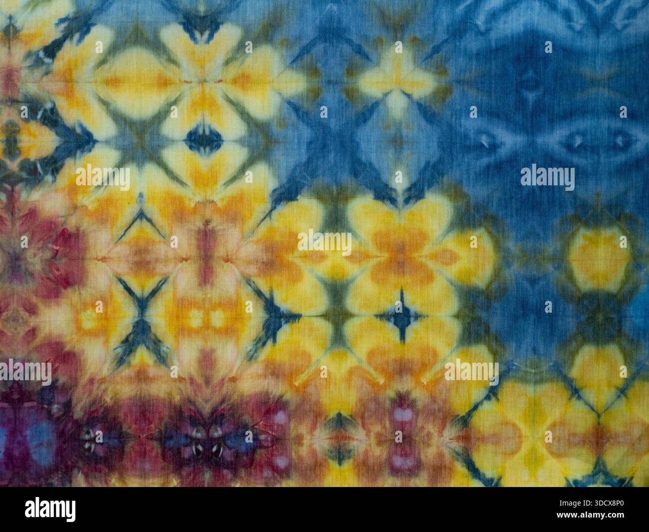 Hand-dyed cotton fabric with a repeating pattern of abstract flowers in yellow and pink against a blue background. Stock Photo