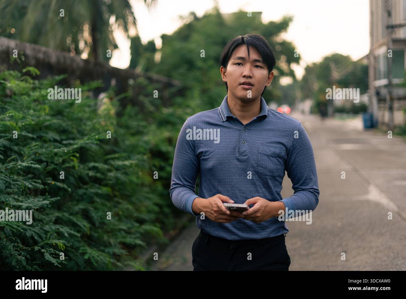 Young asian man standing outdoors holding smartphone, browsing internet Stock Photo