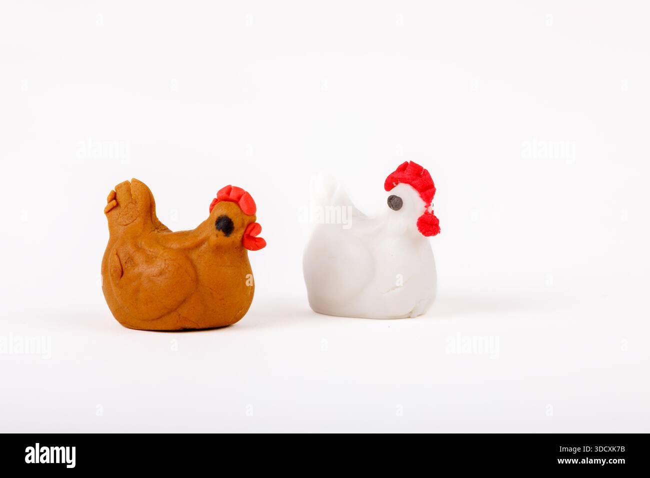 Two handmade marzipan chicken figurines, one white and one brown, isolated on white background. Stock Photo