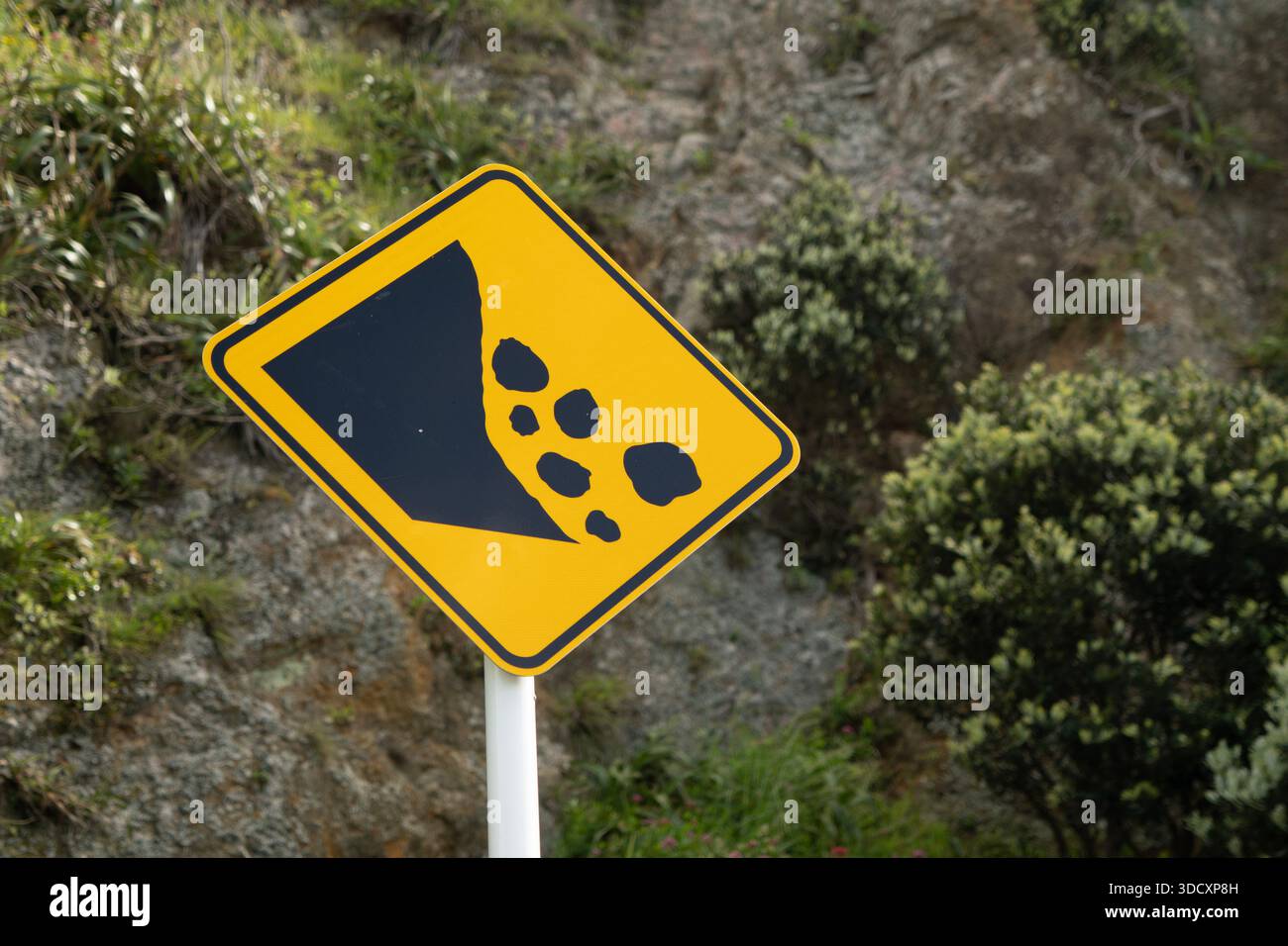 Yellow falling rocks warning sign in front of rock cliff with ...