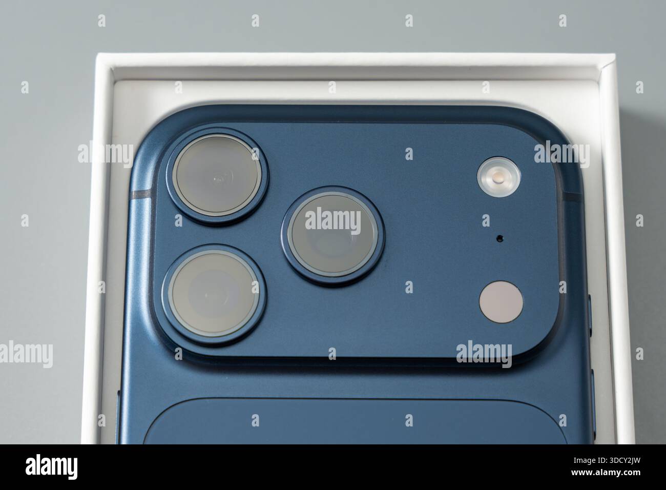 Smartphone placed neatly inside its box, focusing on the rear camera system and smooth finish. Minimalist studio setup highlights product presentation Stock Photo