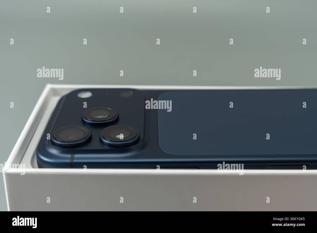 Rear view of a modern smartphone resting in its box, highlighting a triple camera module and clean industrial design. Minimal studio lighting emphasiz Stock Photo
